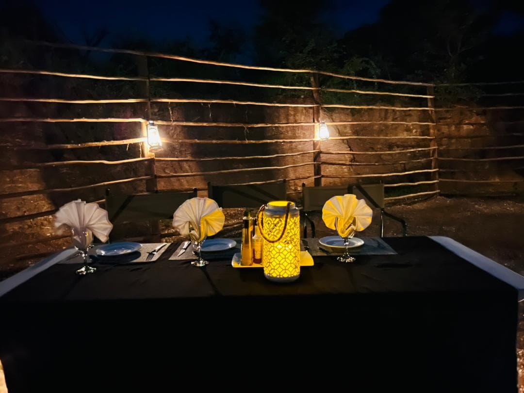 A lantern-lit dinner table set for three in the boma at Xhabe Safari Lodge after dark