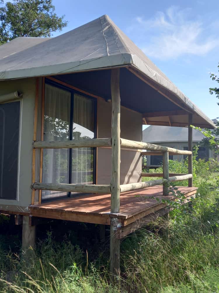 The exterior of a tented chalet raised on stilts, with a wooden deck and gum-pole railing