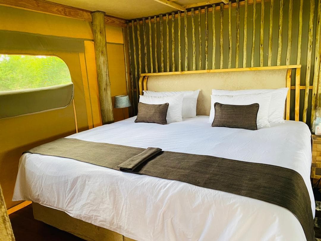 A super king bed made up in a tented chalet, against a wall of gum poles