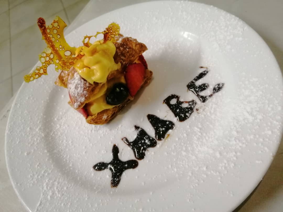 A layered pastry dessert plated with the word Xhabe written in chocolate