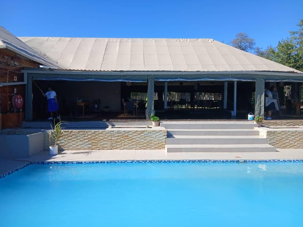 The pool and main building at Xhabe Safari Lodge under a clear blue sky