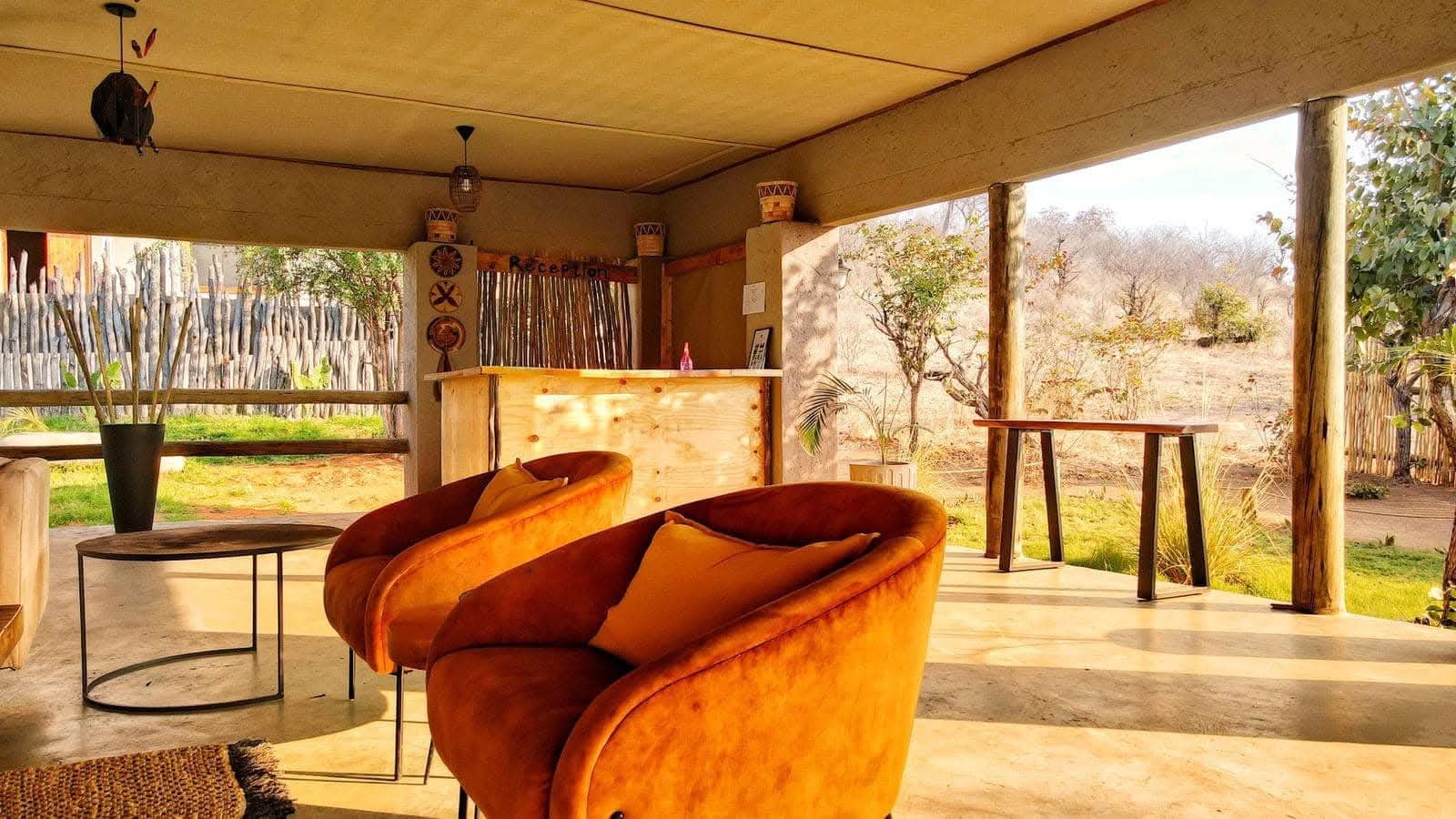 The open-sided reception lounge at Xhabe Safari Lodge in late afternoon light, with burnt-orange velvet armchairs