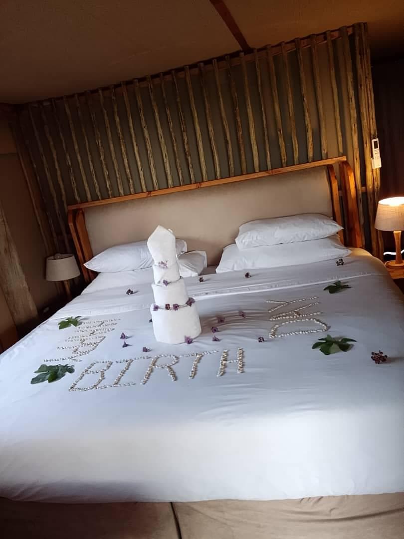 A bed decorated with petals and a towel tower spelling out a birthday message